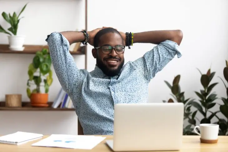 Homme-portant-des-lunettes-souriant-derrière-un-bureau-avec-un-ordinateur-portable Homme portant des lunettes souriant derrière un bureau avec un ordinateur portable