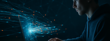 Een persoon die achter een laptop of smartphone zit, met een lichtreflectie van data- of netwerkverbindingen op het scherm.