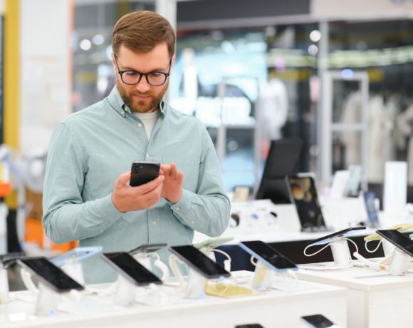 Un homme heureux choisit un téléphone portable dans un magasin d'électronique.